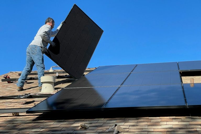 PV-Beratung Handwerker montiert ein Solarpanel auf einem Dach unter klarem blauen Himmel.
